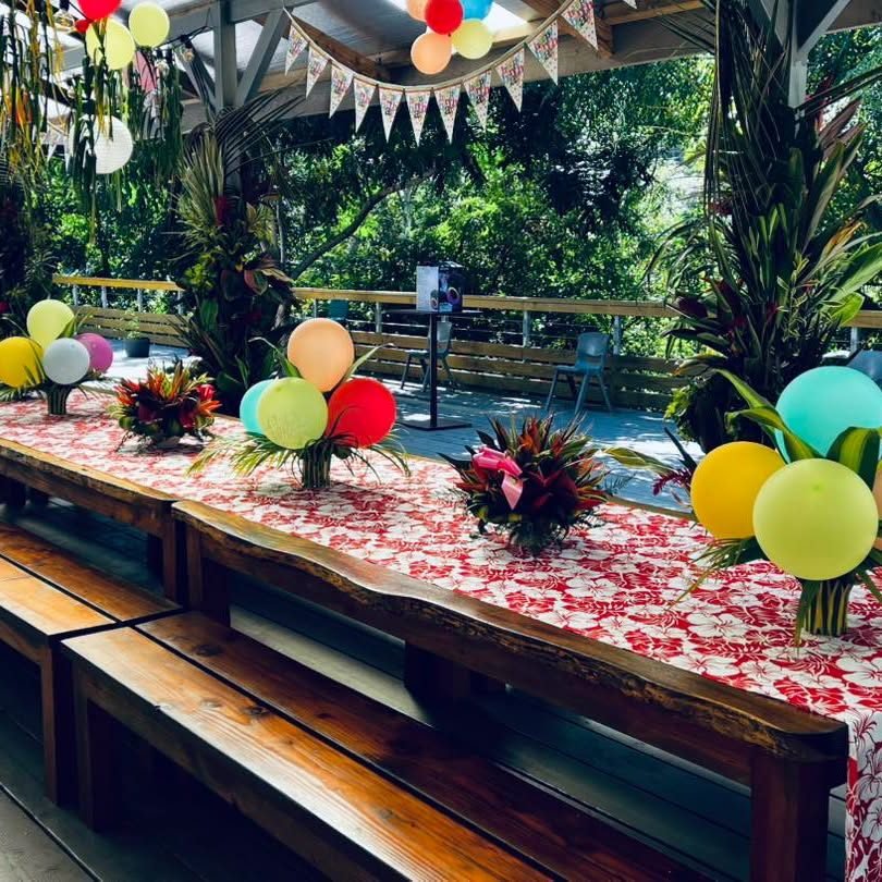 Longue table dressée avec nappe en pareo, ballons et compositions florales